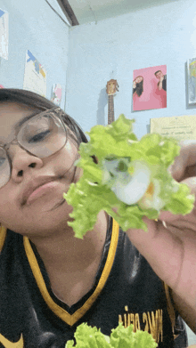 a girl wearing glasses holds a piece of lettuce
