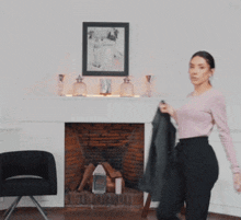 a woman in a pink sweater and black pants is holding a jacket over her head