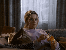 a woman sitting on a couch with a bag of chips in her hand