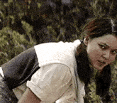 a woman in a white shirt and gray vest is kneeling down in the grass .