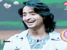 a man with long black hair is smiling in front of a screen that says tanuja