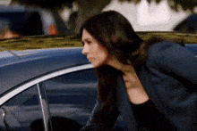 a woman in a suit is standing next to a blue car