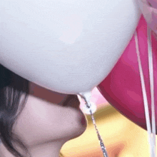 a woman is drinking from a white balloon while holding pink balloons .