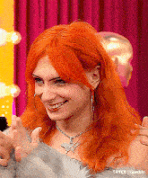 a woman with red hair is wearing hoop earrings and a necklace and smiling .