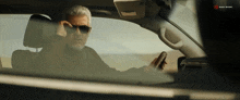 a man wearing sunglasses is driving a car with a sony music logo on the bottom