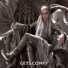a man is sitting on a throne with a crown on his head and the words `` gets comfy '' .