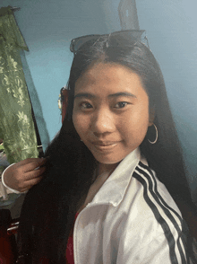 a girl wearing sunglasses and a white adidas jacket looks at the camera