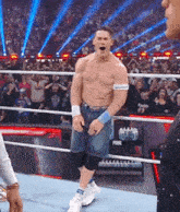 a shirtless wrestler is standing in a wrestling ring in front of a crowd .