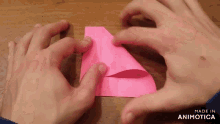 a person is folding a piece of pink paper with the words made in animotica visible