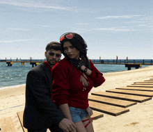 a man in a suit and a woman in a red sweater pose on a beach