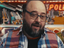 a man wearing glasses and a plaid shirt is standing in front of a sign that says poli