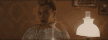 a woman in a white dress is sitting next to a lamp in a dark room .