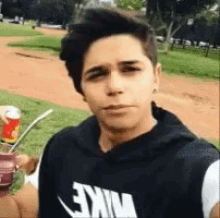 a young man wearing a nike hoodie is holding a straw and drinking from a can .