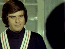 a man wearing a black turtleneck and striped sweater is looking at himself in the mirror