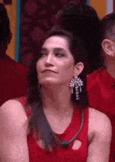 a woman in a red dress and earrings is sitting in front of a crowd .