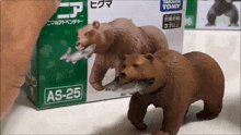 a toy bear with a fish in its mouth is in front of a box that says as-25