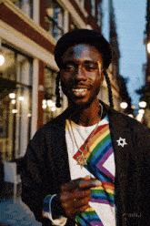 a man wearing a black hat and a rainbow shirt with a star necklace