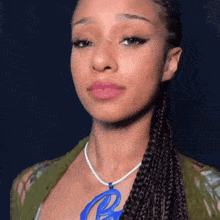 a woman wearing a braided ponytail and a necklace with a blue pendant .
