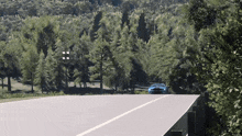 a blue car is driving down a road in a forest