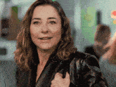 a woman in a black leather jacket is smiling and holding her purse