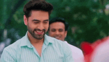a man with a beard is smiling and looking at the camera while standing in front of a group of people .
