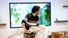 a man standing next to a skeleton in front of a large screen .
