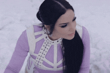 a woman wearing a purple top and a white harness stands in the snow