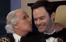 a man in a tuxedo kisses another man on the cheek while they pose for a picture