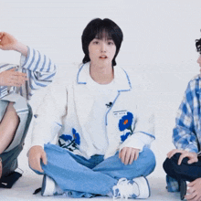 a group of young men are sitting on the floor and one of them is wearing a white jacket with blue flowers on the front