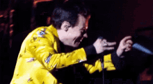 harry styles is wearing a yellow jacket and singing into a microphone on stage .