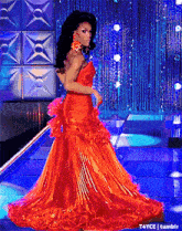 a woman in a red dress is standing in front of a blue curtain ..