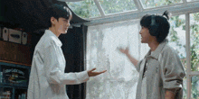 two men are standing next to each other in front of a window .