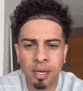 a man with curly hair and a beard is wearing a grey shirt and earrings