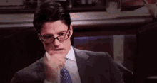 a man in a suit and tie is sitting in a dark room with his hand on his chin .