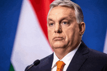 a man in a suit and tie stands in front of a flag