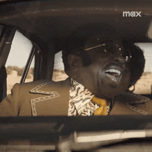 a man in a suit and tie is laughing in a car with the word max on the bottom right