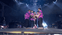 a group of people standing on a stage with one wearing a purple shirt
