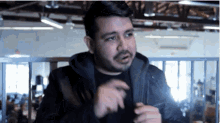 a man with a beard is wearing a black jacket and a black shirt and is standing in a room .
