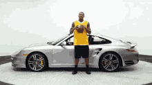 a man in a yellow jersey is holding a basketball in front of a silver sports car