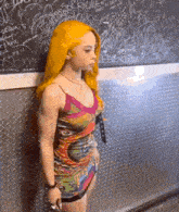 a woman in a colorful dress stands in front of a wall with graffiti on it including the word richie