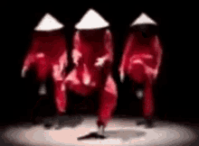 a group of people wearing red jumpsuits and white hats are dancing on a stage .