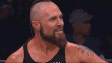 a man with a beard is wearing a black tank top and has a tattoo on his shoulder