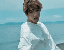 a man in a white shirt stands in front of the ocean