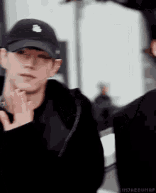 a man wearing a black hat and a black jacket is standing next to another man and waving .