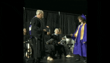 a man in a graduation cap and gown is shaking hands with a woman in a purple gown .