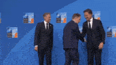 three men in suits are shaking hands in front of a wall that says nato otan