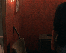 a young man standing in a dark room with a red wall behind him