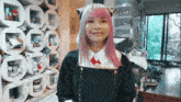 a girl with pink hair and cat ears is smiling in front of a stack of shelves