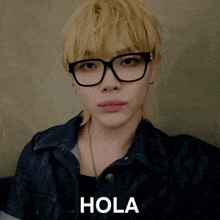 a man wearing glasses and a denim jacket has the word hola written on his face