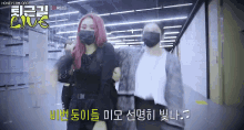 two women wearing face masks are standing next to each other in a hallway .